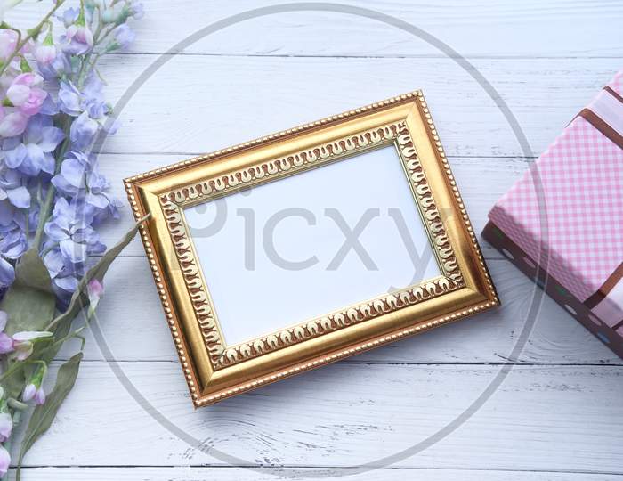 Empty Picture Frame, Gift Box And Flower On Table.