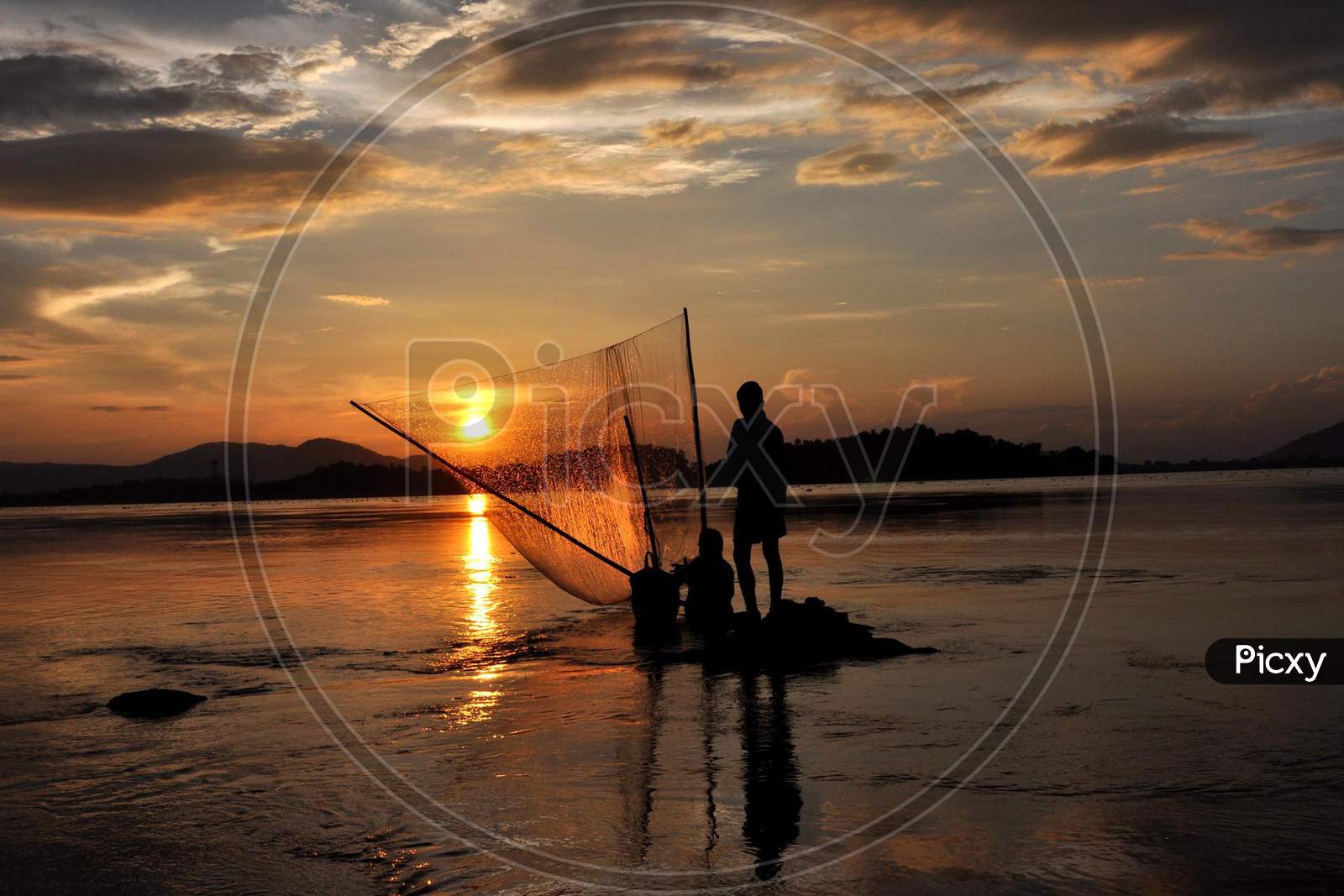 Fisherman Catches Fish At The Banks Of The Brahmaputra River  During Sunset In Guwahati, India