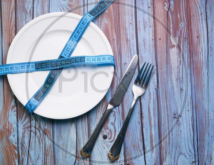 Clean Plate With Measurement Tape And Cutlery On Wooden Background