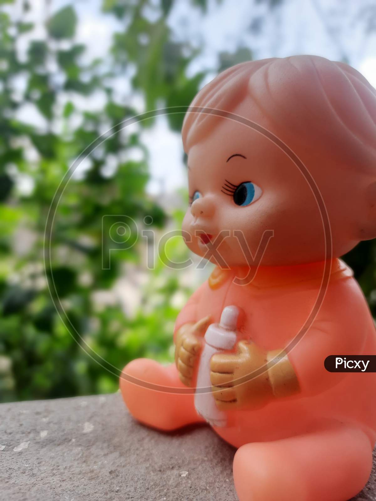a baby toy with blue eyes small nose and mouth having a bottle of milk holded in hands in blur greenish background