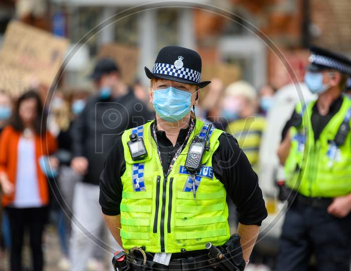 A Female Police Officer Wears A Ppe Face Mask At A Black Lives Matter Protest With Out Of Focus Protesters In The Background
