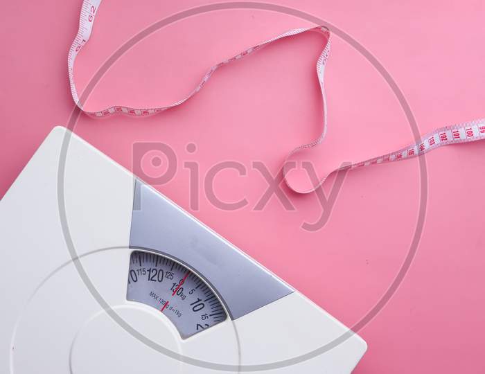 A Tape Measure And Bathroom Scale On Pink Background