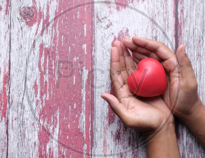 Man Holding Red Heart In Hands On Wooden Table .
