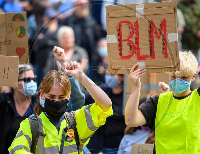 Caucasian Protesters Wear Ppe Face Masks, Salute And Hold A Homemade Blm Sign At A Black Lives Matter Protest
