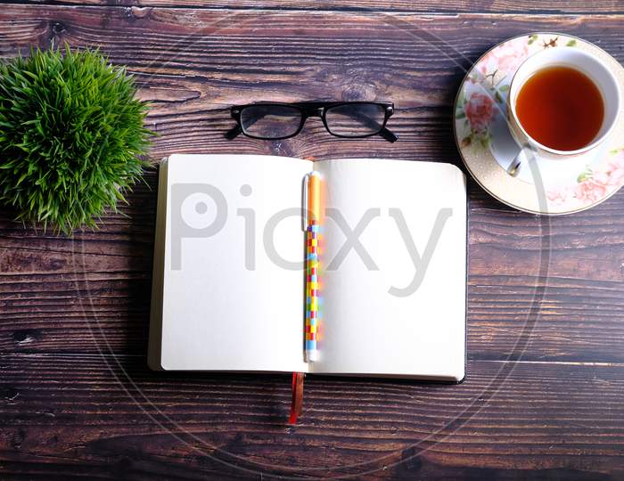 High Angle View Of Open Diary, Tea And Eyeglass On Table