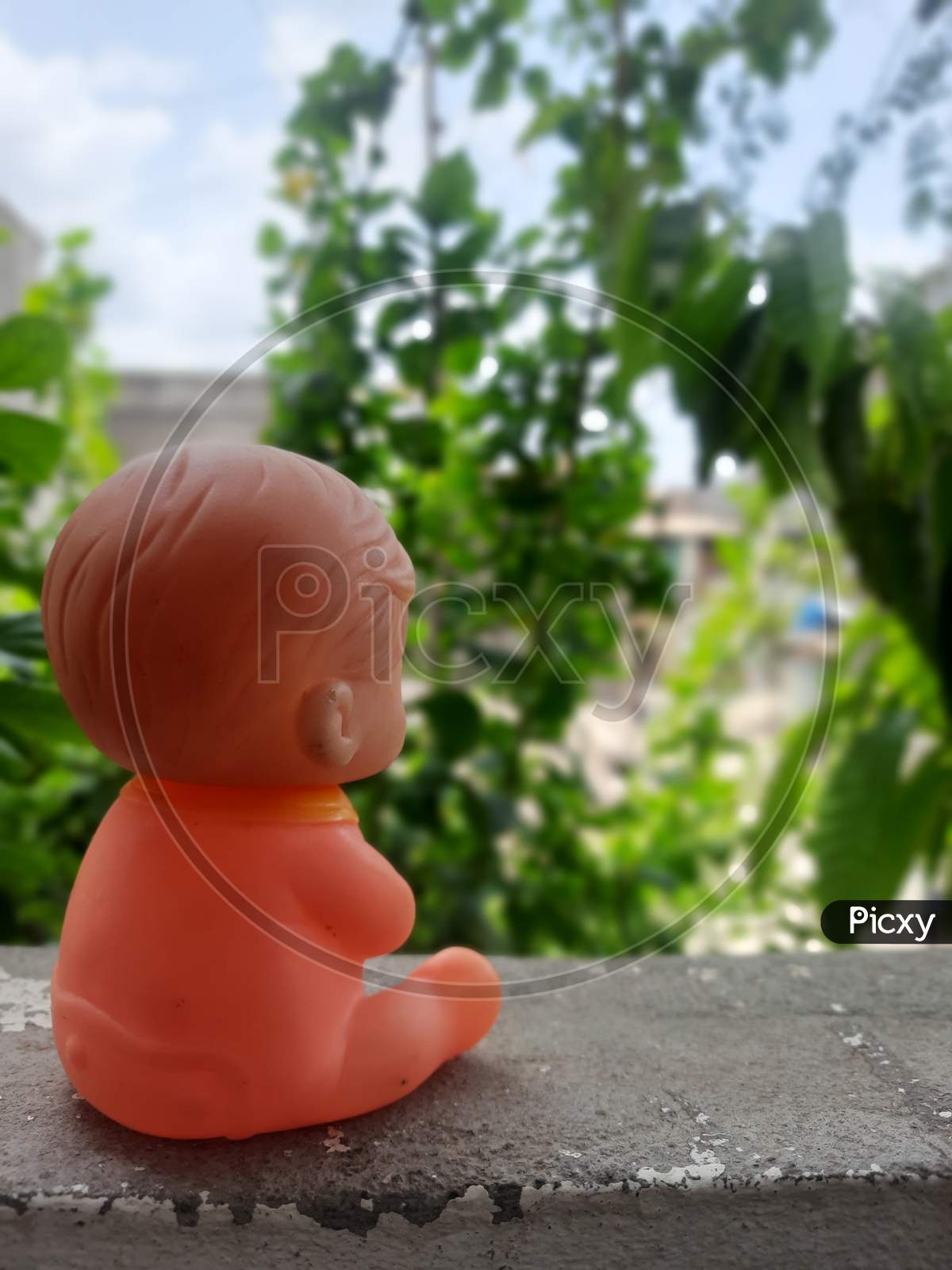 a sad baby toy sitting angry watching the greenery, tress and leaves