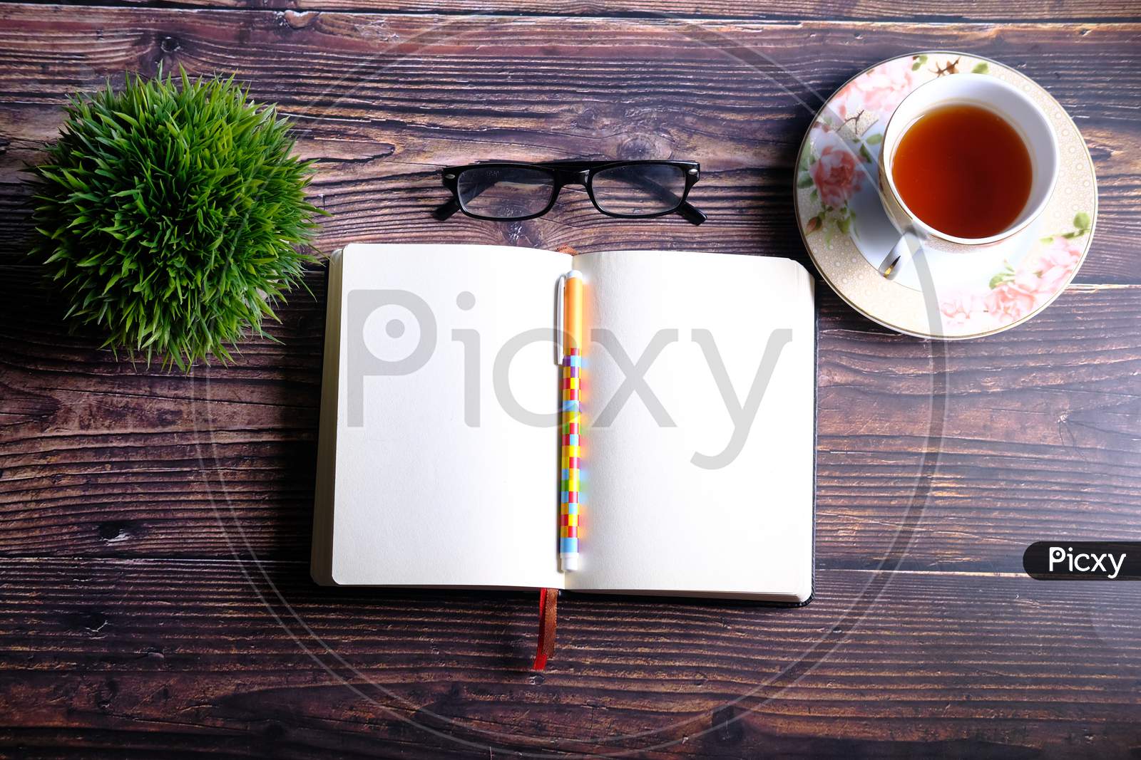 High Angle View Of Open Diary, Tea And Eyeglass On Table