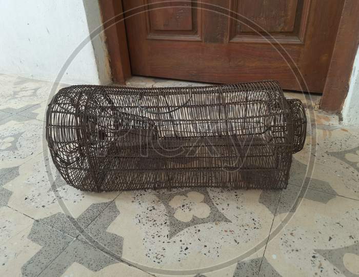 a old rusted mouse trap or cage on the designer floor, a door in background