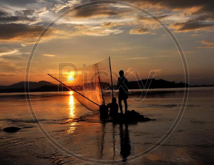 Fisherman Catches Fish At The Banks Of The Brahmaputra River  During Sunset In Guwahati, India