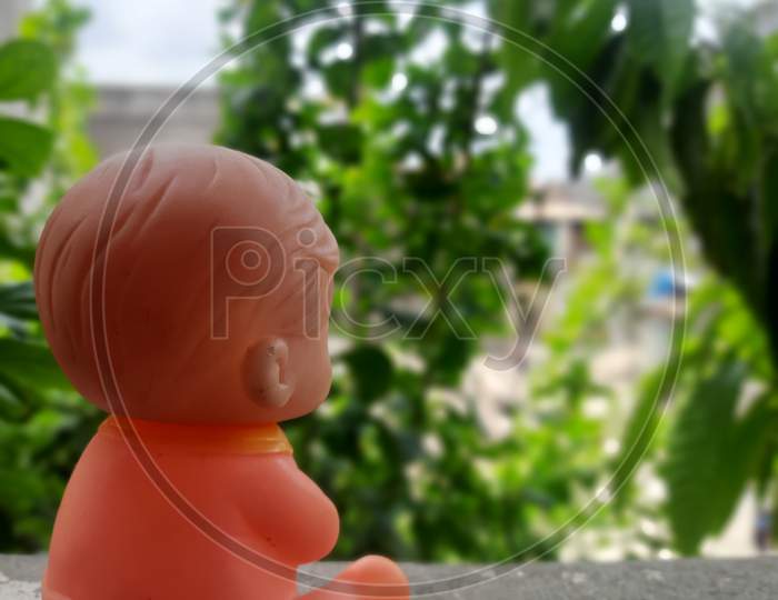 a sad baby toy sitting angry watching the greenery, tress and leaves