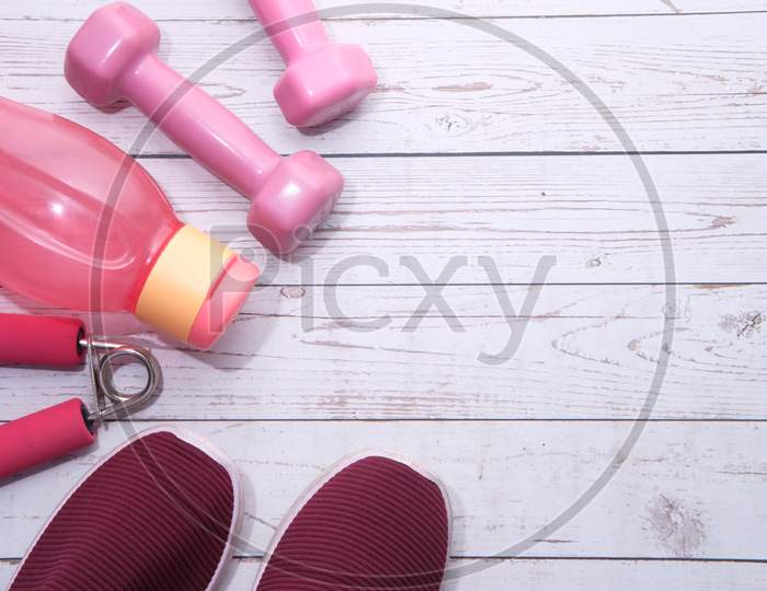 Top View Of Dumbbell, Shoe And Water Bottle On Pink Background