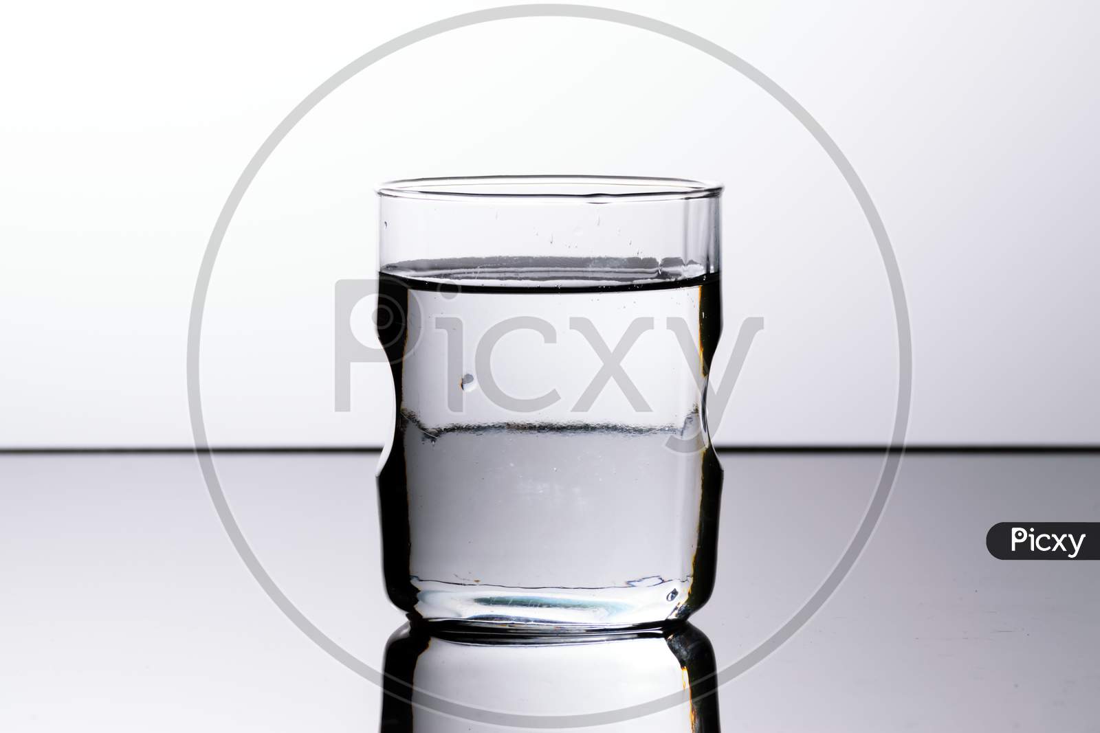 A Glass Of Transparent Water Kept On A Reflective Surface In A White Background