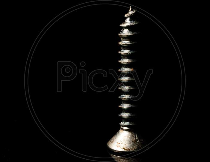 An Isolated Screw Placed On A Reflective Surface With A Dark Background