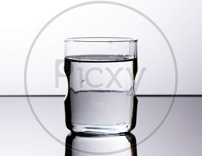 A Glass Of Transparent Water Kept On A Reflective Surface In A White Background