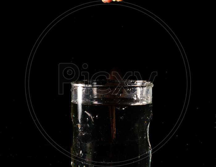 A Glass Of Water Placed On A Reflective Surface In A Dark Background And A Piece Of Cut Lemon Is Being Squeezed From Above