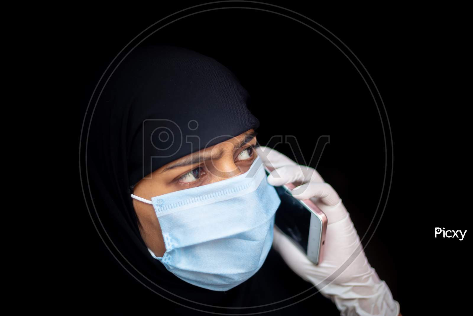 A Muslim Girl Wearing A Safety Mask And Gloves Is Talking On Her Smartphone. Black Hijab Woman Wearing A Blue Mask For Coronavirus Safety.
