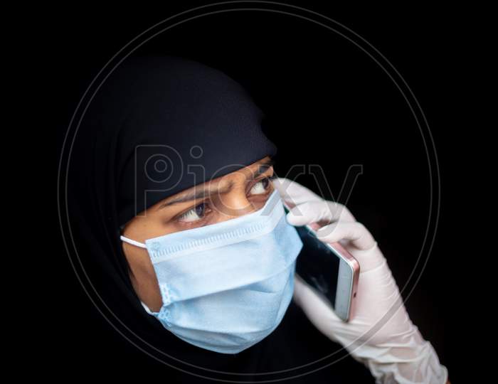 A Muslim Girl Wearing A Safety Mask And Gloves Is Talking On Her Smartphone. Black Hijab Woman Wearing A Blue Mask For Coronavirus Safety.