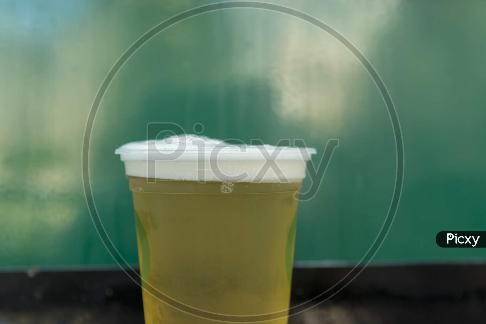 Close Up Of Cold Beer In Plastic Glass On Green Background