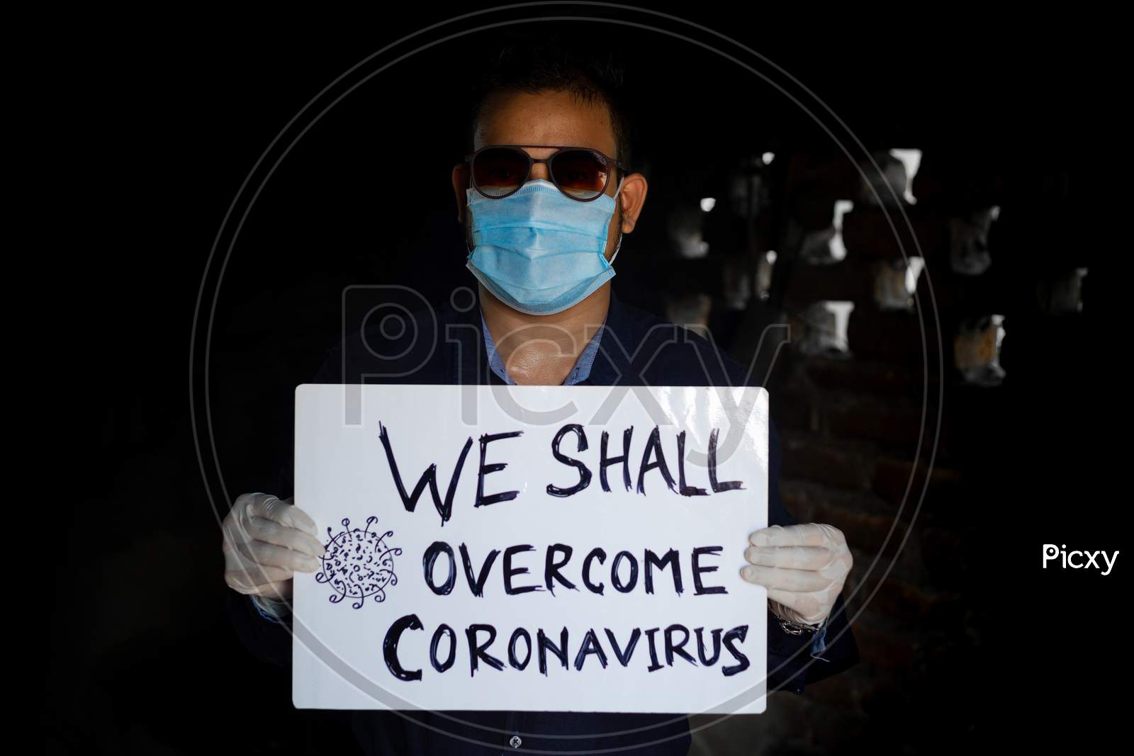 A Young Man Wearing A Medical Mask And Safety Gloves Stands With A Placard Message To "We Shall Overcome Coronavirus". A Man Holding A Placard Massage.