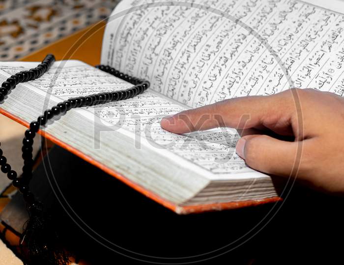Muslim Woman Reading The Holy Quran Using The Finger. The Holy Quran On The Mat Of Prayers . Close-Up Views. Indoors. Focus On Hands.
