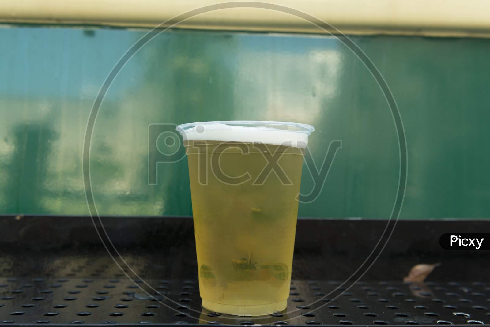 Close Up Of Cold Beer In Plastic Glass On Green Background