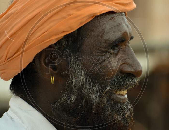 Side pose of black beared person with turban on his head.