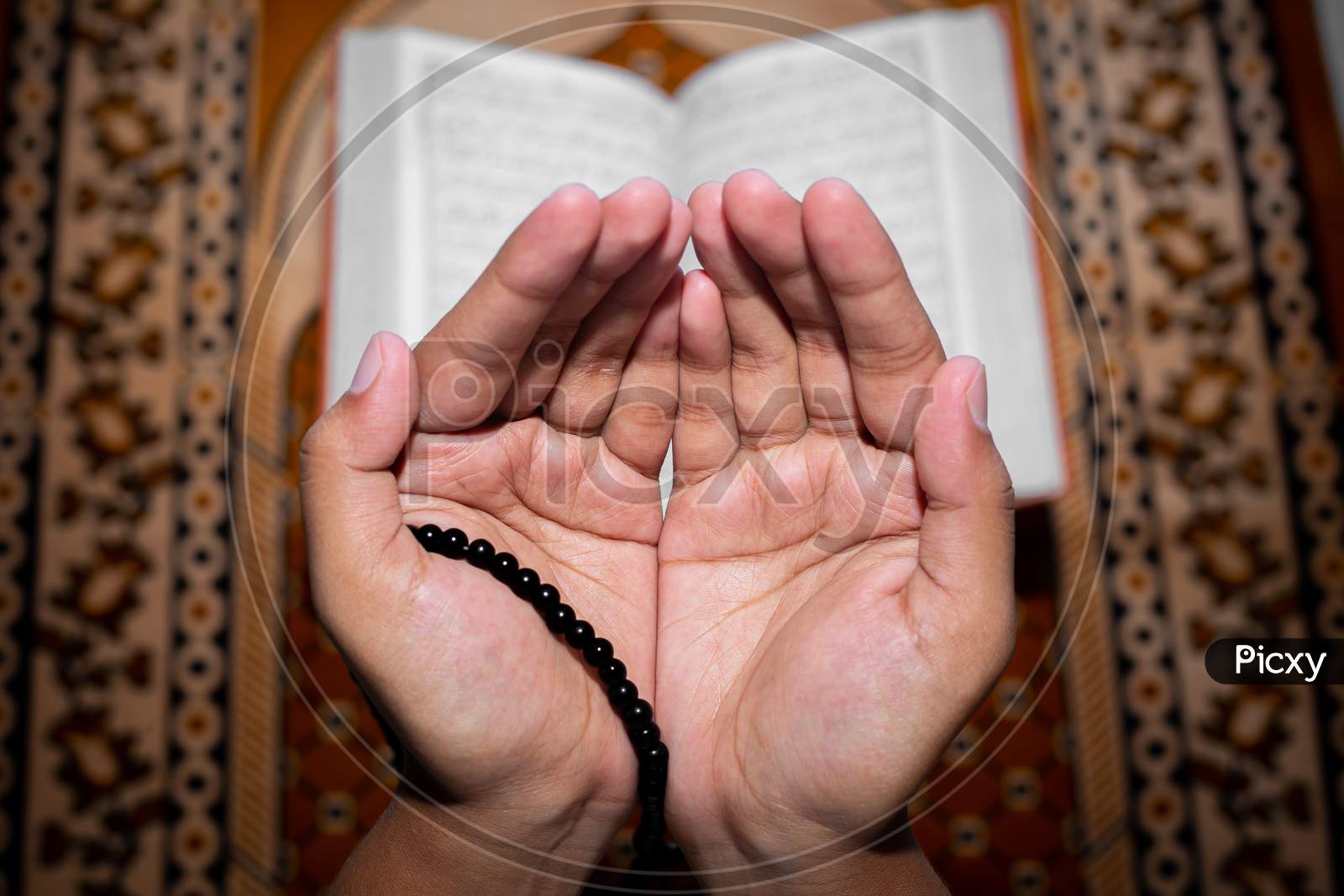 Young Muslim Woman Praying With Tasbeeh. The Holy Quran Is The Background, Indoors. Focus On Hands.