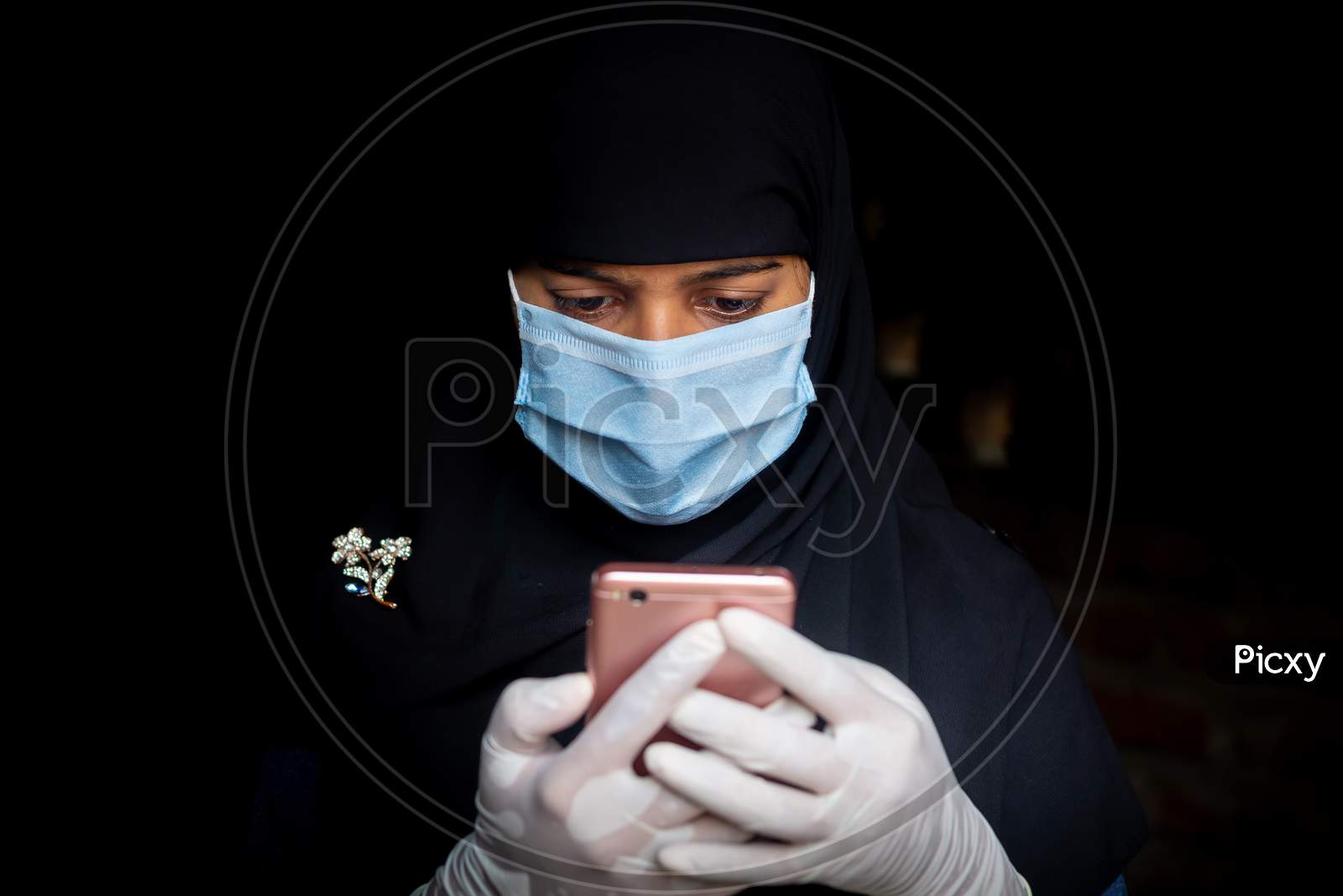 A Safety Mask-Wearing An Asian Muslim Girl Is Using His Smartphone. Black Hijab Woman Wearing A Blue Mask For Coronavirus Safety.