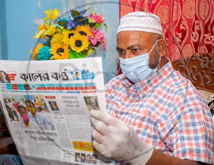 Bangladesh – June 05, 2020: A Mature Man Reading On The News Of The Coronavirus Epidemic In A Local Newspaper Wearing A Surgical Mask And Medical Gloves At Joypara, Dhaka.
