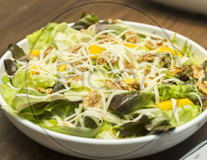 Closeup Of Delicious Salad Of Lettuce, Watercress, Arugula, Mango, Walnuts And Shredded Cheese.