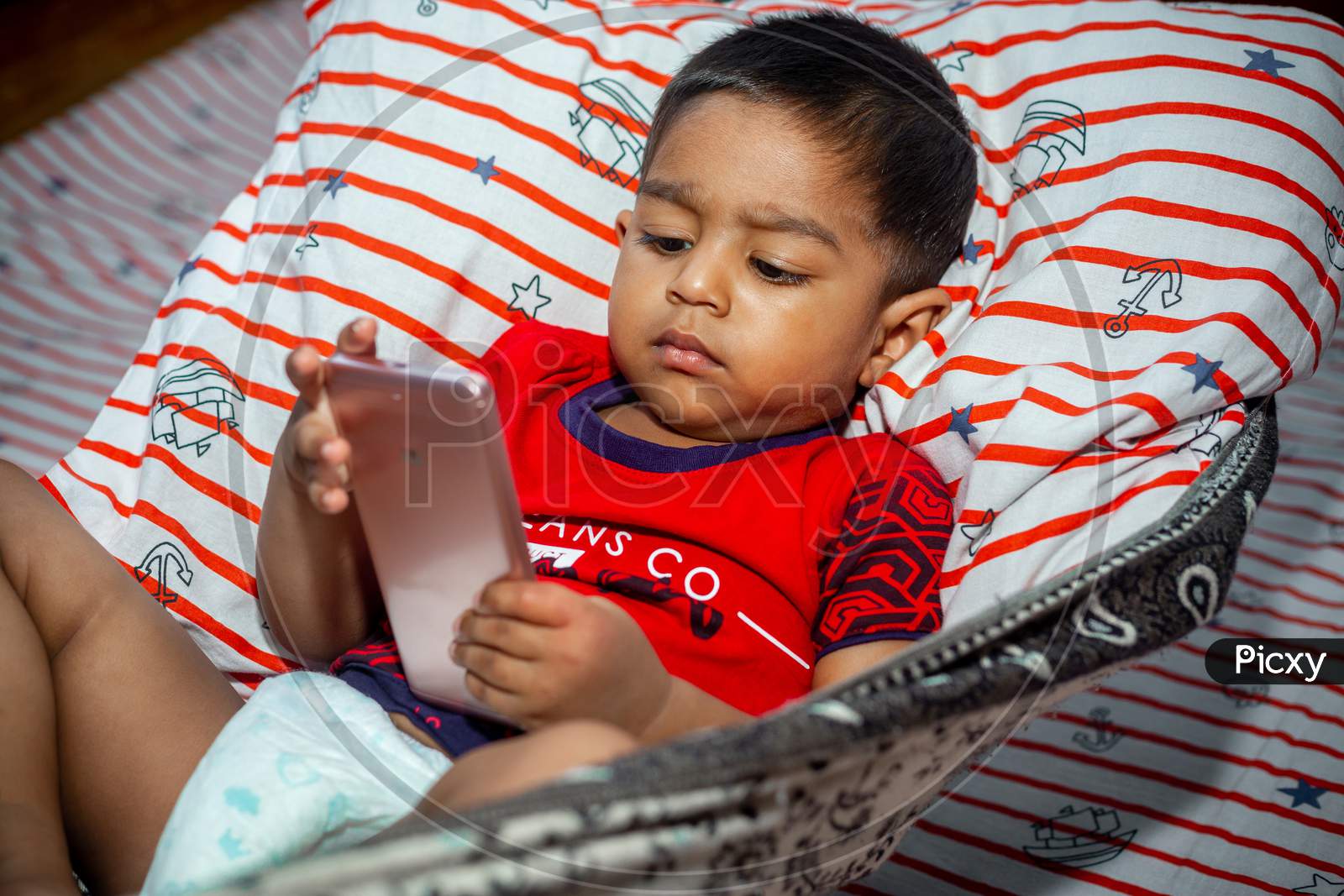 Before Going To Sleep A Child Is Lying A Homemade Hammock And Watching Cartoons Using A Smartphone. Kids Playing With Smartphone. Mobile Phone And Internet Addiction Concept.