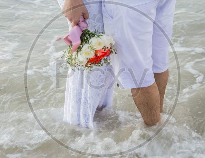 Bride Holding Bouquet Of Flowers With Her Feet Submerged In Sea Water