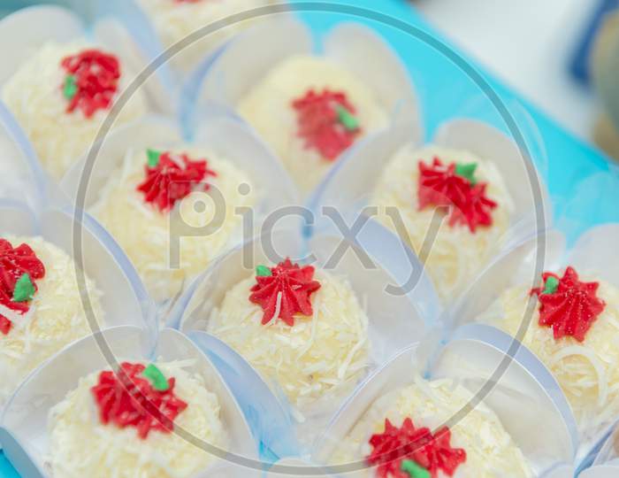 Coconut Candy With Icing Grated Coconut And Red Cream Into Paper Box On Blue Tray.