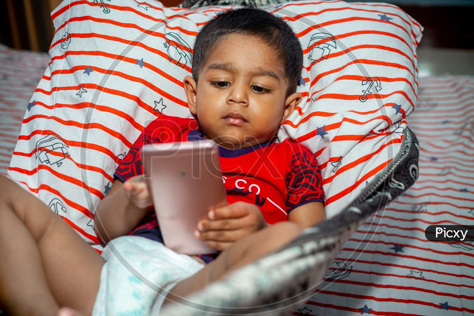 Before Going To Sleep A Child Is Lying A Homemade Hammock And Watching Cartoons Using A Smartphone. Kids Playing With Smartphone. Mobile Phone And Internet Addiction Concept.