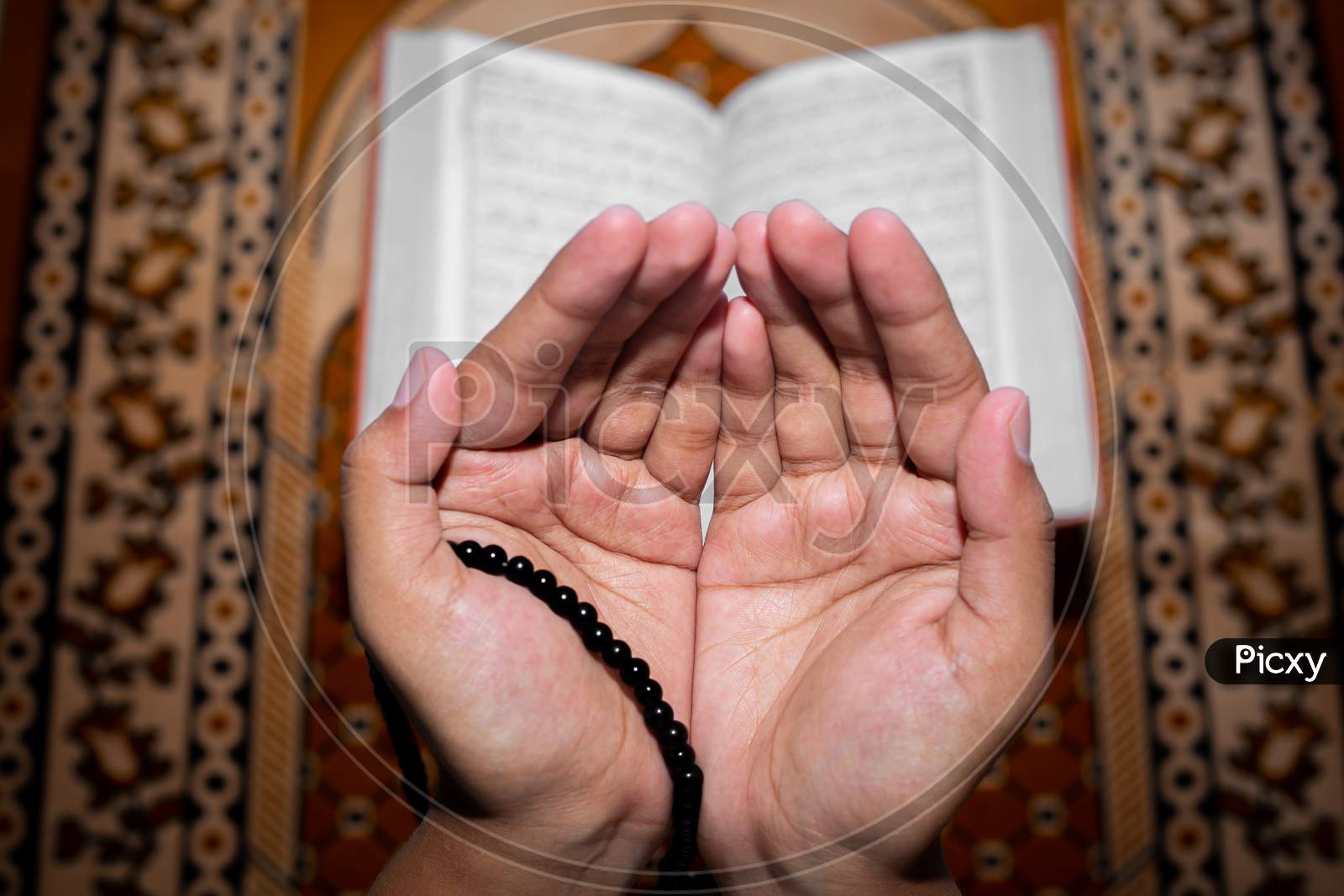 Young Muslim Woman Praying With Tasbeeh. The Holy Quran Is The Background, Indoors. Focus On Hands.