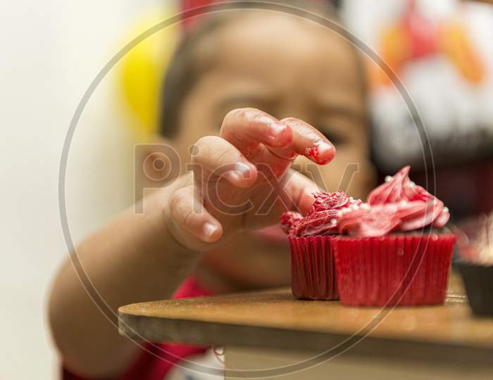 Blurred Image Of A Boy Picking Up A Creamy, Red Cupcake.