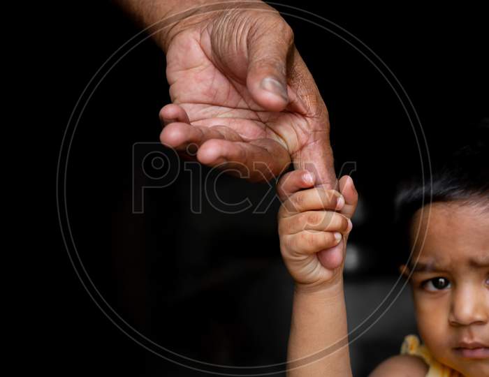 A Baby Boy Confidently Walks Around Holding On The Finger Of A Senior Old Man. Family, Generation, Support And People Concept. Dark Background.