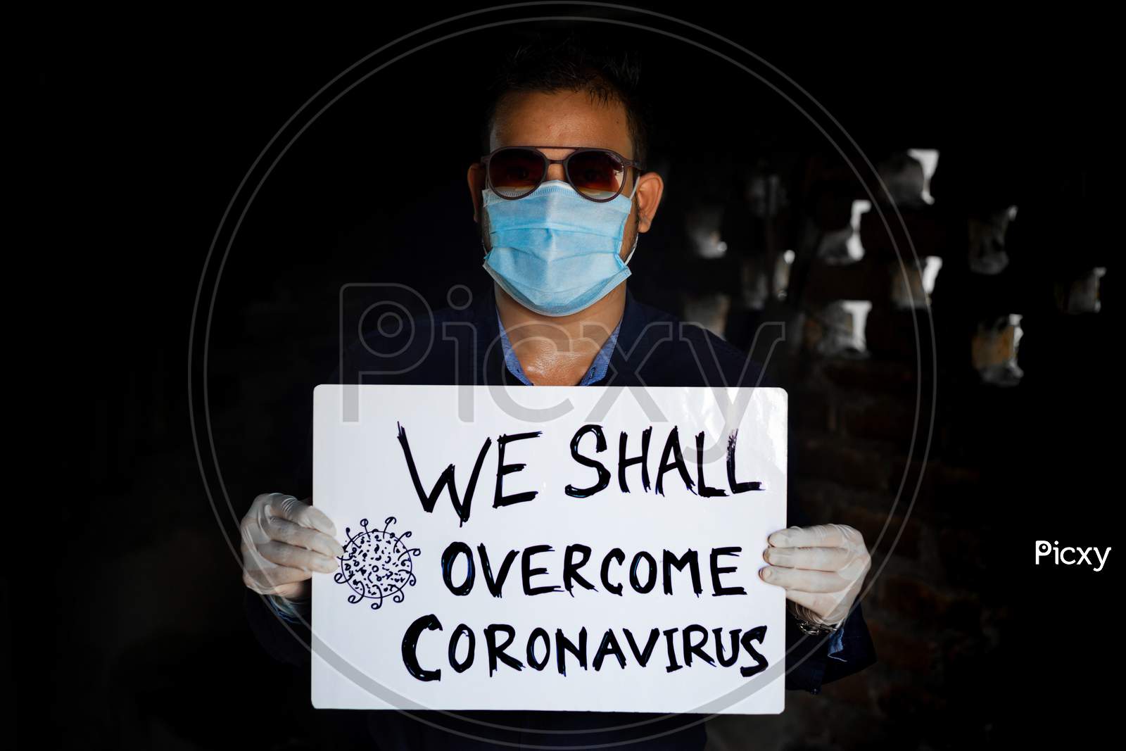 A Young Man Wearing A Medical Mask And Safety Gloves Stands With A Placard Message To "We Shall Overcome Coronavirus". A Man Holding A Placard Massage.