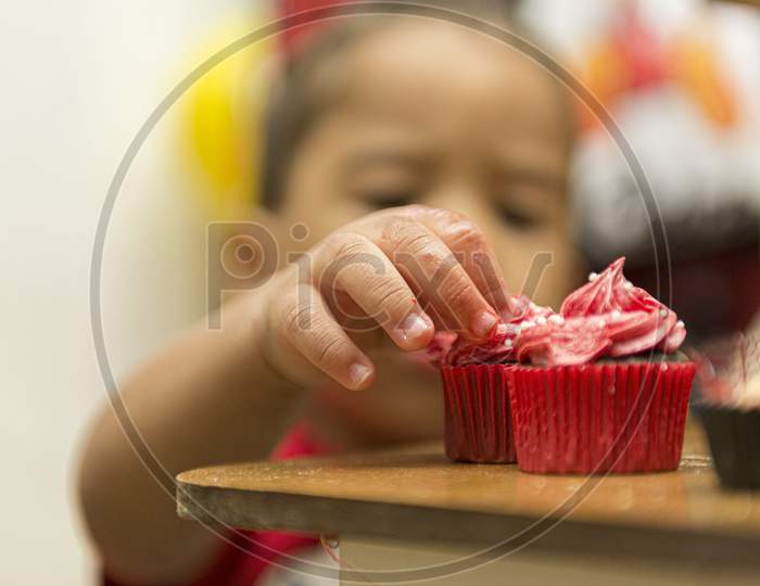 Blurred Image Of A Boy Picking Up A Creamy, Red Cupcake.