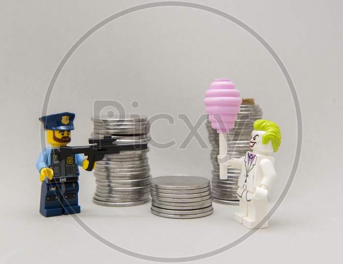 Policeman Aiming His Firearm At The Joker Next To A Pile Of Coins.