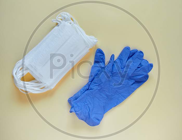 Antiviral Surgical Ear-Loop 3-Layer Masks And A Pair Of Gloves For Protection Against Corona Virus And Bacteria. Medical Protective Masks And Gloves On Yellow Background. Protection Concept