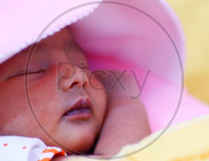 A Newborn Asian Baby Wrapped In Pink Hooded Towel And Sleeping With Eyes Closed