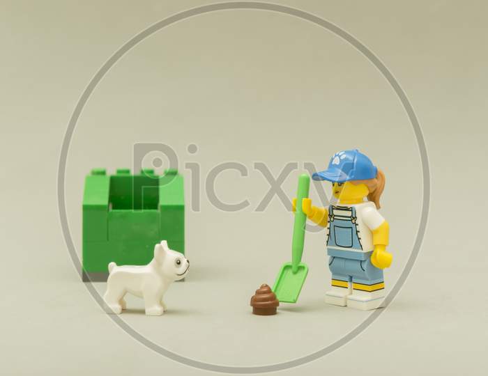 Woman Holding A Shovel Next To A Green Trash Bin Looking For Her Dog Poop.