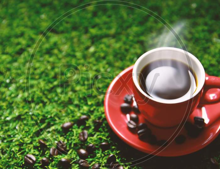 Red Coffee Cup On The Green Grass With Copy Space For Text Or Advertising, Drinking Concept, Love Concept, Relax Concept, Selective Focus On Edge Of Cup
