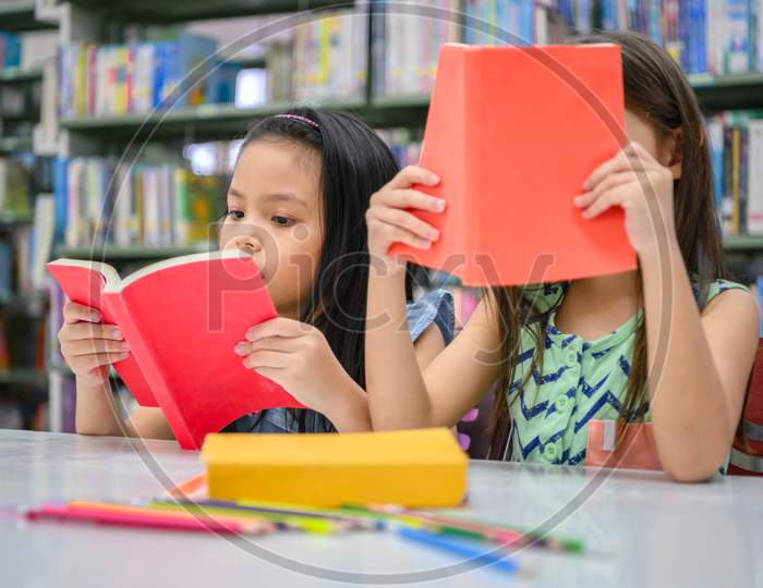 Two Little Cute Girls Multi-Ethnic Friends Reading Books Together In School Library. People Lifestyles And Education Learning Concept. Happy Friendship Kids Doing Leisure Activity For Examination Test
