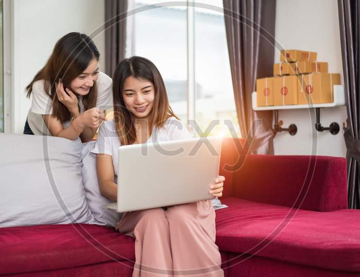 Two Young Freelancer Asian Girl Businesswomen Private Working At Home Office With Laptop Computer Sitting On Sofa. Packaging Delivery Online Shopping Service And Marketing Advertising To Customer