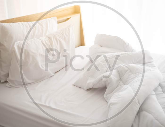 White Unmade Bed In The Morning With Sunshine With White Curtain Background In Elegant Home. Interior Design And Luxury Furniture Concept. Indoors Lifestyle And Lazy Activity Theme.