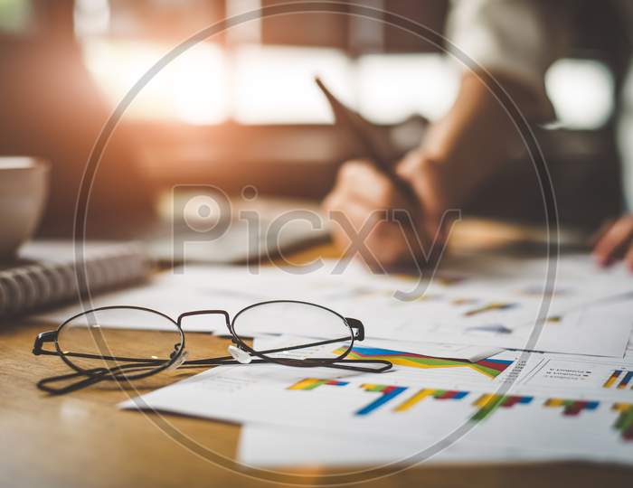 Close Up Of Glasses With Businesswoman  Writing Summary Report Data In Background. Marketing And Business Ownership Concept. People And Lifestyles Concept. Business Employee And Financial Theme.