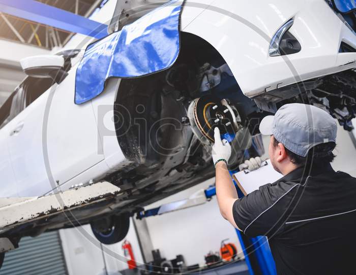 Asian Male Car Technician Car Maintenance For Customers According To Specified Vehicle Maintenance Checklist. Disk Brake Pad Wear Automotive Repairing On Vehicle. Safety Inspection Check Service