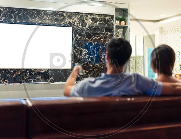 Asian Couples Watching White Blank Screen Display Television For Advertising Template Background.  People Lifestyles Concept. Lockdown Social Distancing Work From Home. Selective Focus On Tv